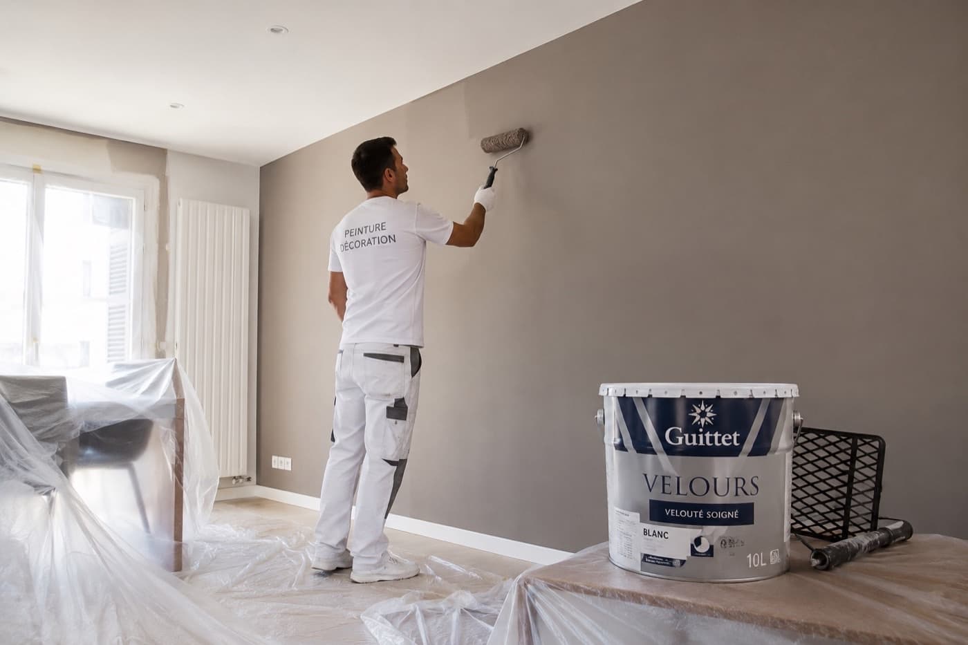 Peintre appliquant une peinture taupe au rouleau dans un salon
